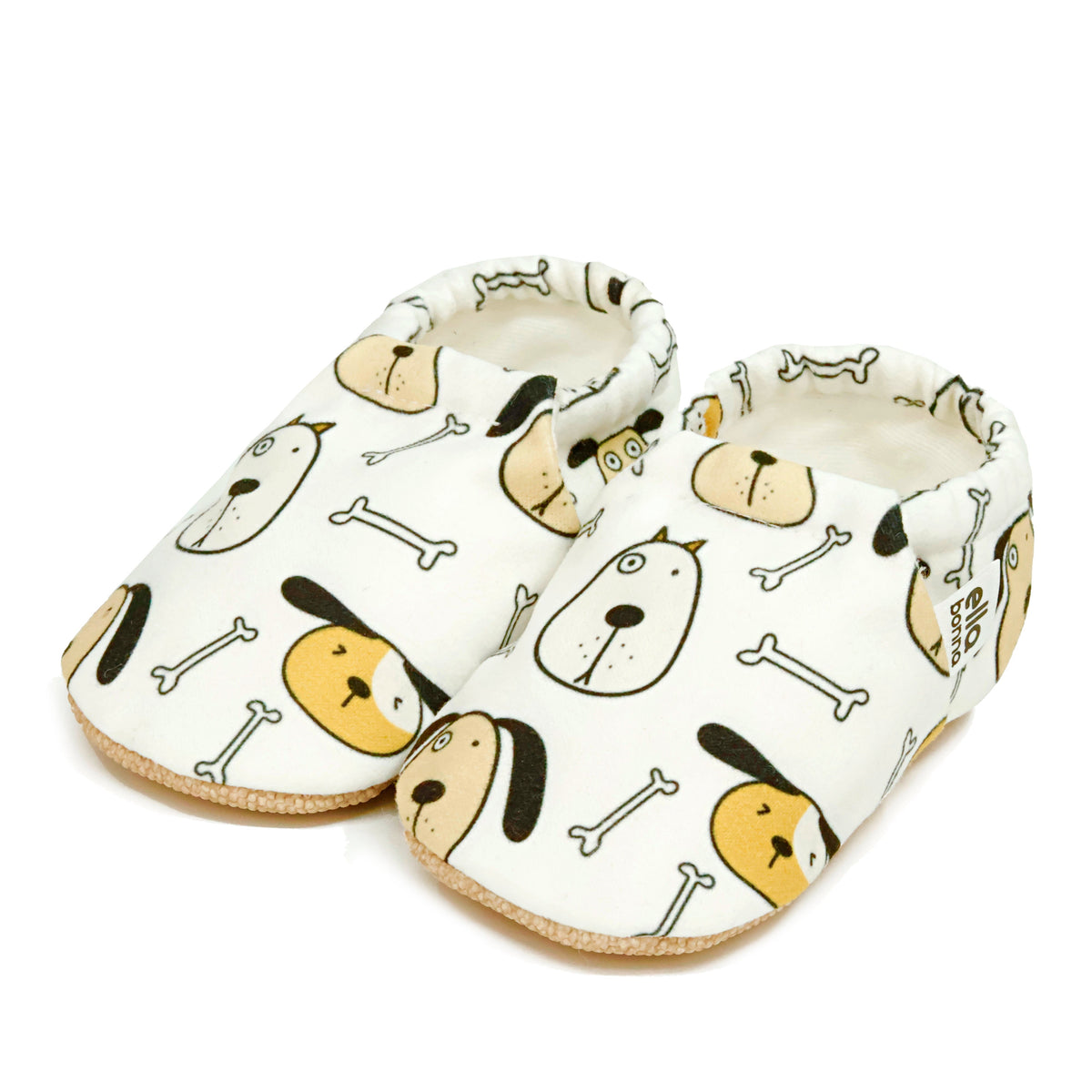 Pair of cream slip-on baby moccasins with dog faces and bone print on a white background.
