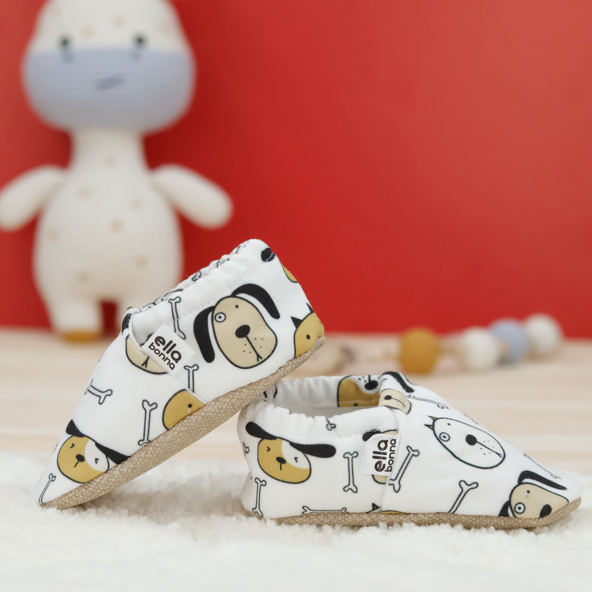 Cream slip-on baby moccasins with dog faces and bone print arranged together to show the sides and uppers.