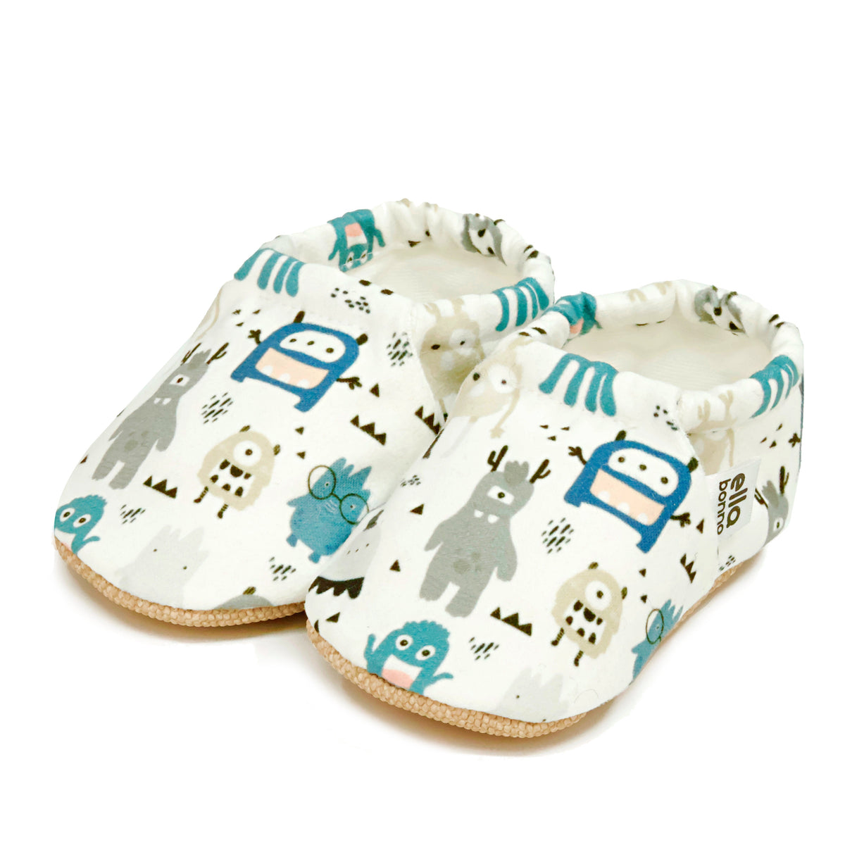 Pair of cream slip-on baby moccasins with blue-and-gray cartoon monster print on a white background.