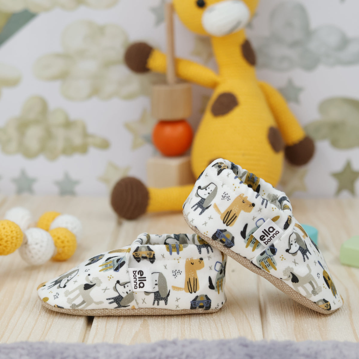 Cream slip-on baby moccasins with yellow, blue and gray dog print arranged together to show the sides and uppers.
