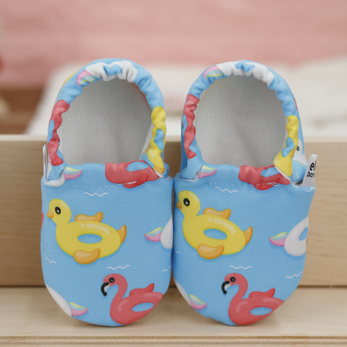 Pair of blue slip-on baby moccasins with colorful duck, swan and flamingo pool-float print, showing the openings and uppers.