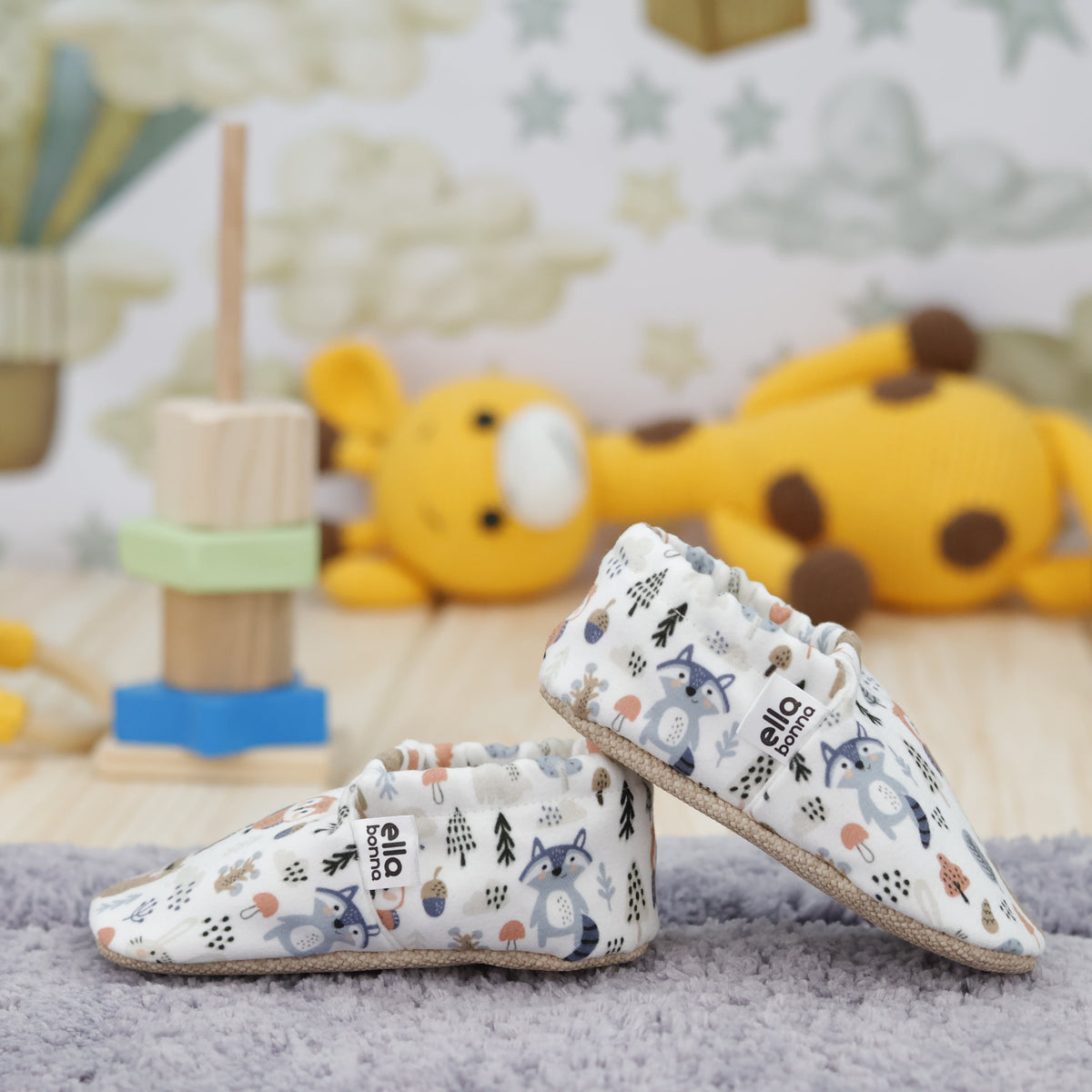 Cream slip-on baby moccasins with woodland animal and tree print arranged together to show the sides and uppers.