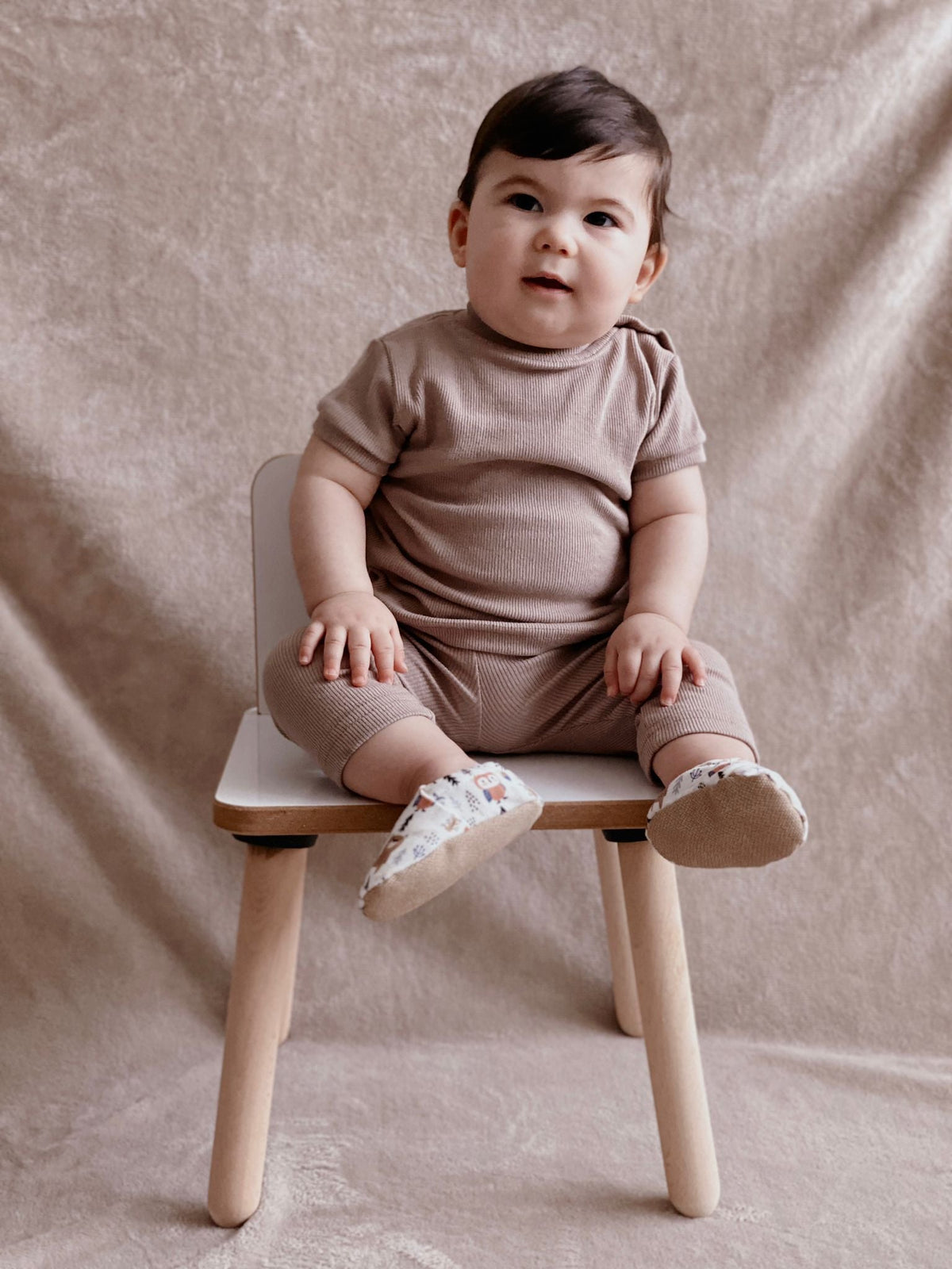 Child seated on a stool wearing woodland-print moccasins.