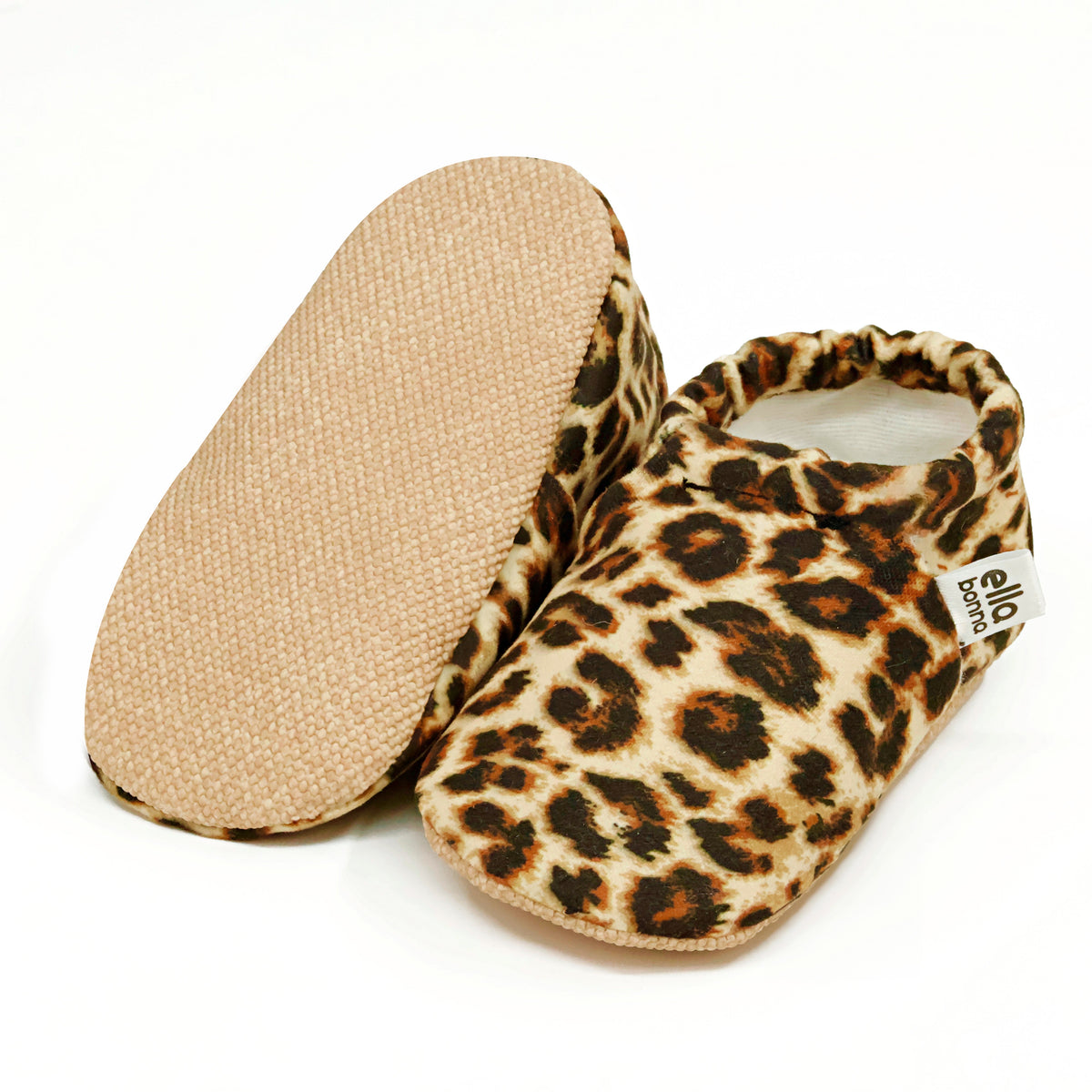 Tan slip-on baby moccasins with brown-and-black leopard spots, with one sole facing the camera on a white background.