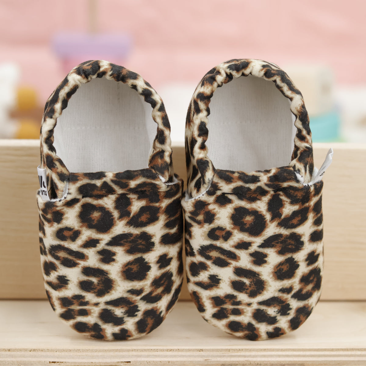 Pair of tan slip-on baby moccasins with brown-and-black leopard spots, showing the openings and uppers.