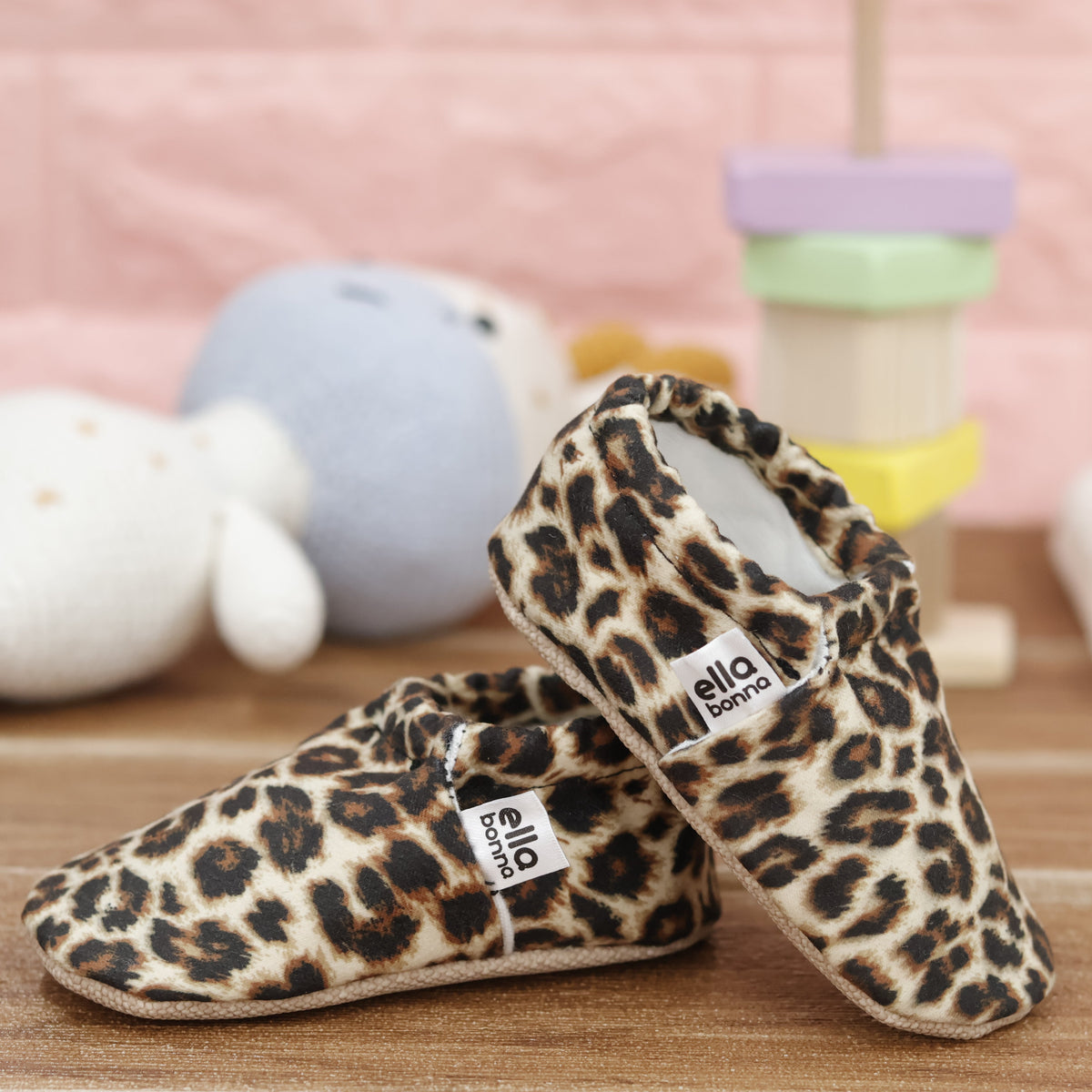 Tan slip-on baby moccasins with brown-and-black leopard spots arranged together to show the sides and uppers.