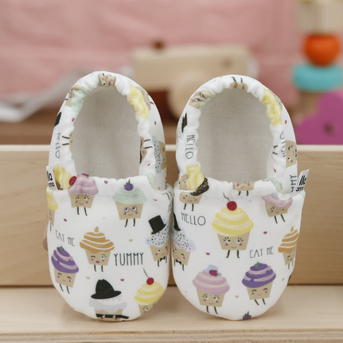 Pair of cream slip-on baby moccasins with pastel cupcake print, showing the openings and uppers.