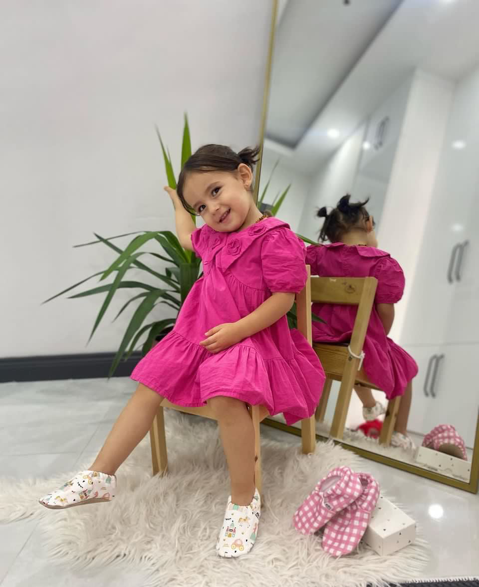 Child in a pink dress seated wearing princess-print moccasins.