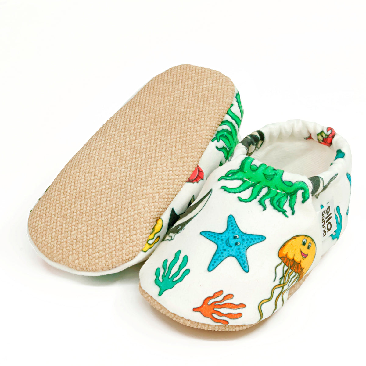 Cream slip-on baby moccasins with colorful sea animals and starfish, with one sole facing the camera on a white background.