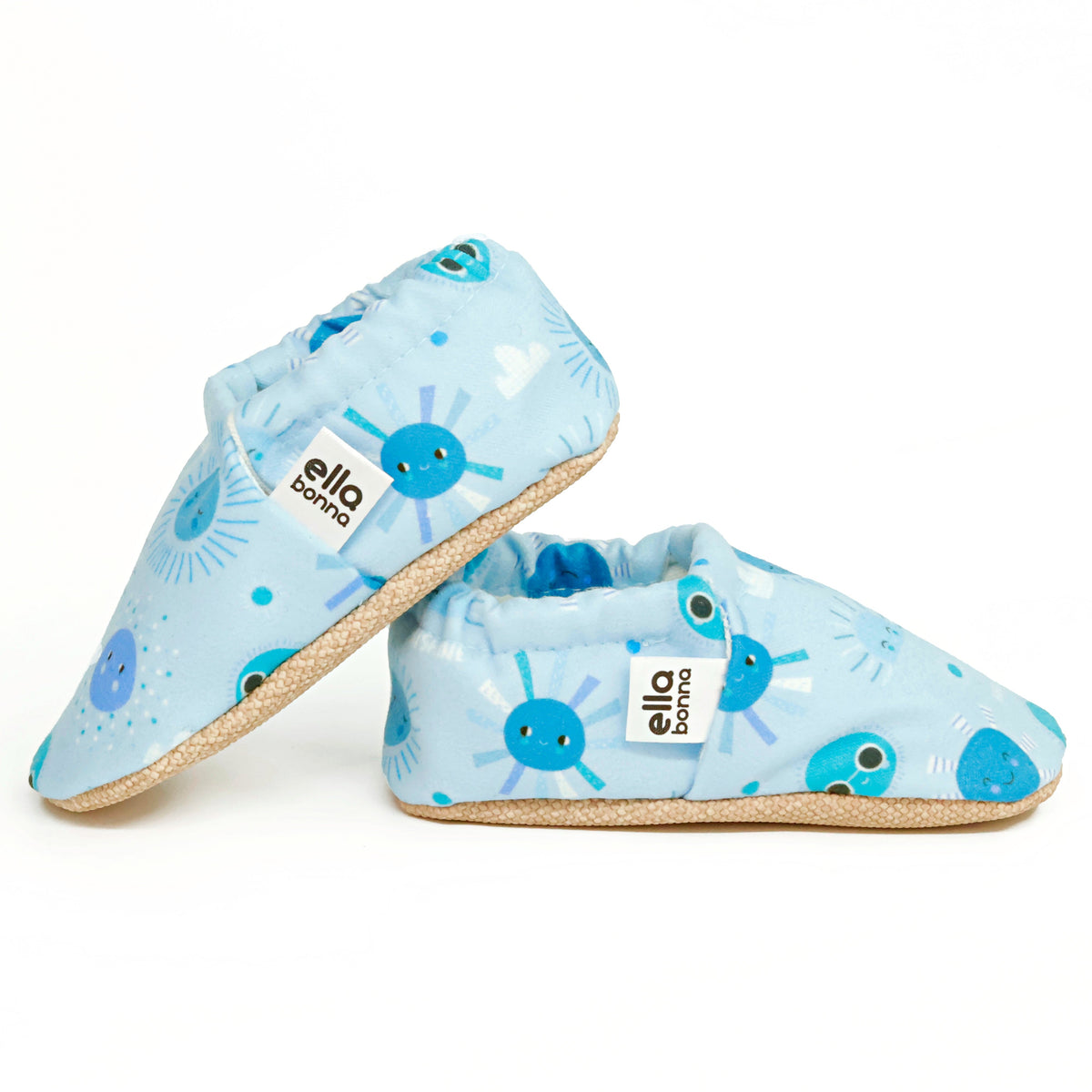 Side views of light blue slip-on baby moccasins with blue sun and moon print on a white background.