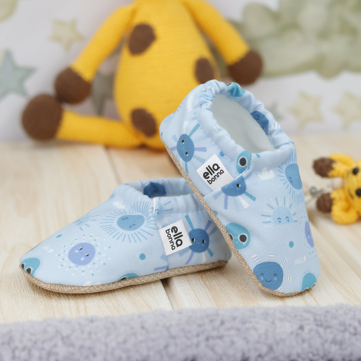 Light blue slip-on baby moccasins with blue sun and moon print arranged together to show the sides and uppers.