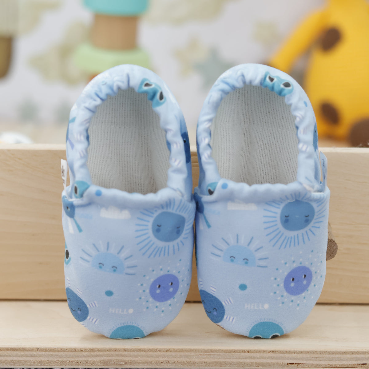 Pair of light blue slip-on baby moccasins with blue sun and moon print, showing the openings and uppers.