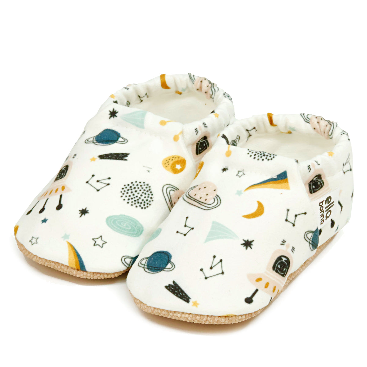 Pair of cream slip-on baby moccasins with planets, rockets and constellation print on a white background.