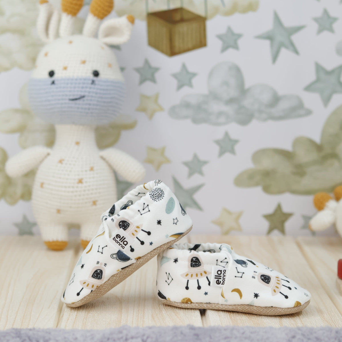 Cream slip-on baby moccasins with planets, rockets and constellation print arranged together to show the sides and uppers.