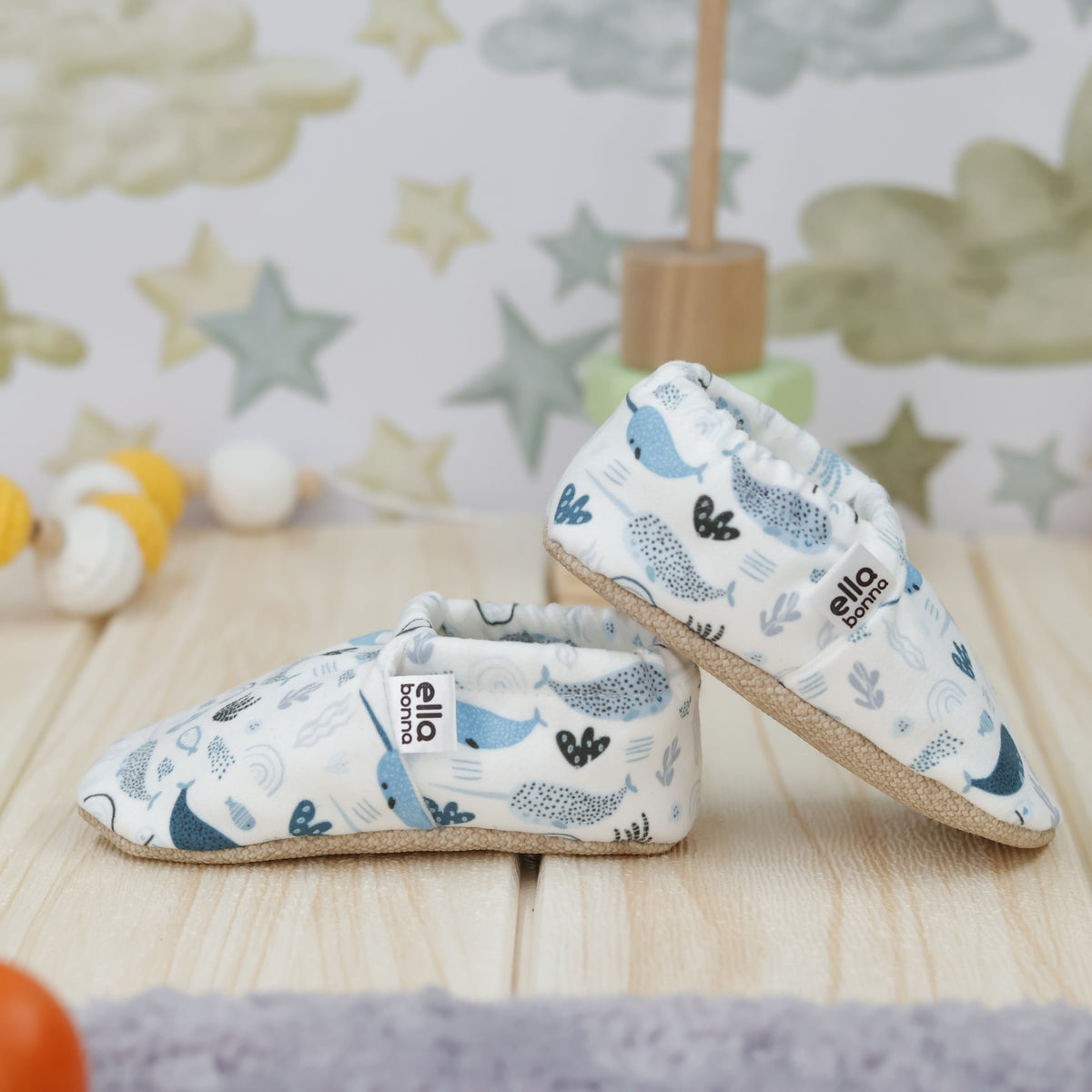Cream slip-on baby moccasins with blue sea-creature print arranged together to show the sides and uppers.