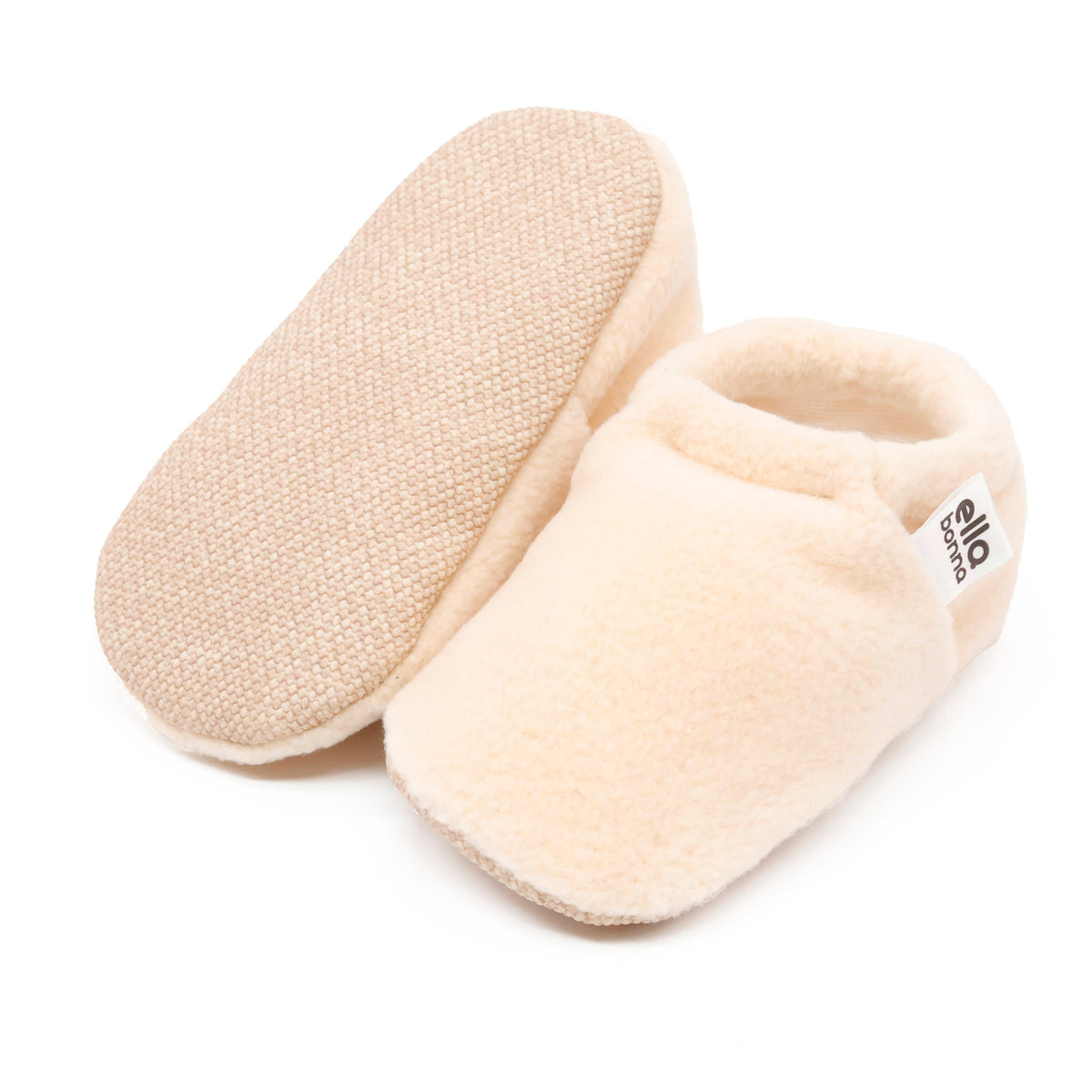 Cream fleece slip-on baby moccasins with tan soles, with one sole facing the camera on a white background.