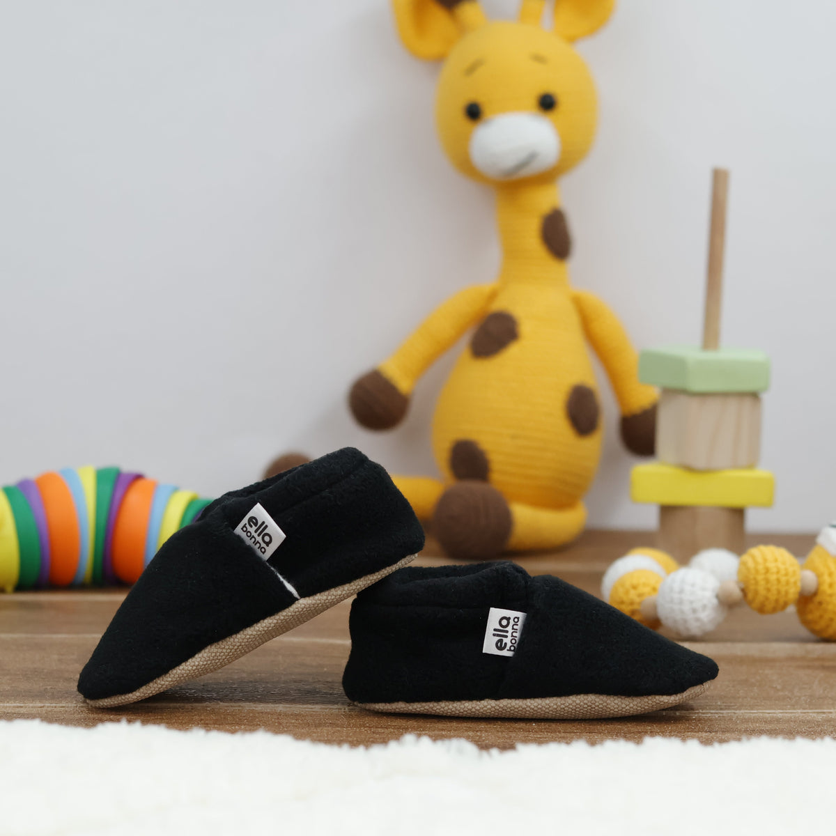 Black fleece slip-on baby moccasins with tan soles arranged together to show the sides and uppers.