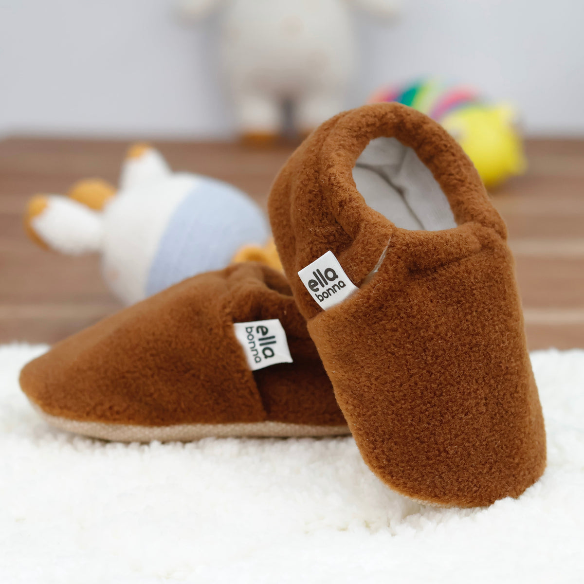 Warm brown fleece slip-on baby moccasins with tan soles arranged together to show the sides and uppers.