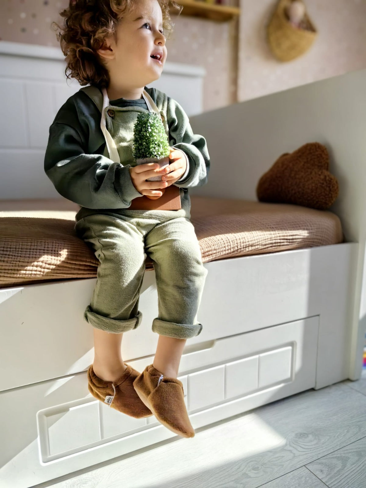Child seated on a window seat wearing brown fleece moccasins.