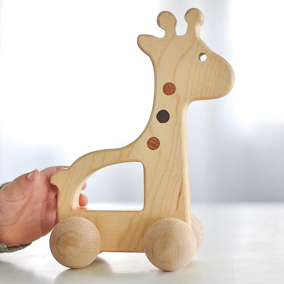 Hand beside the giraffe push toy, showing its wooden body, spots and wheels