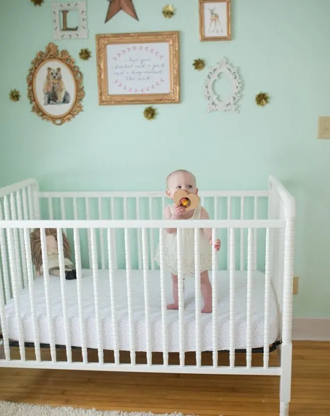 Wide nursery view with a child and a wooden heart rattle near the crib