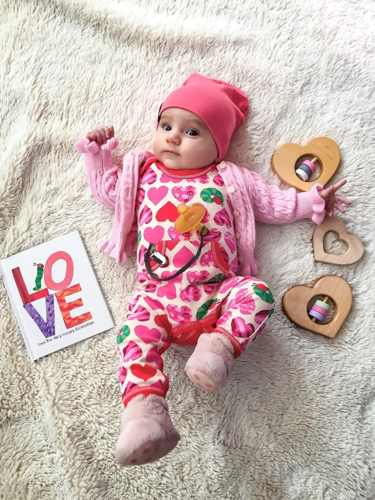 Baby beside several heart-shaped wooden rattles and grasping toys