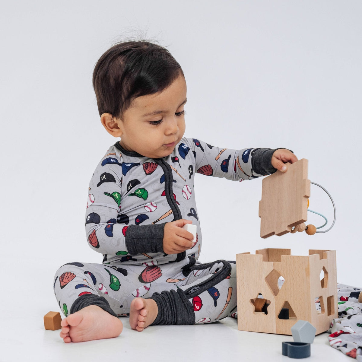 Baby lifting the lid of a wooden toy while wearing Bam & Stitch Major League Buddies Convertible Romper.