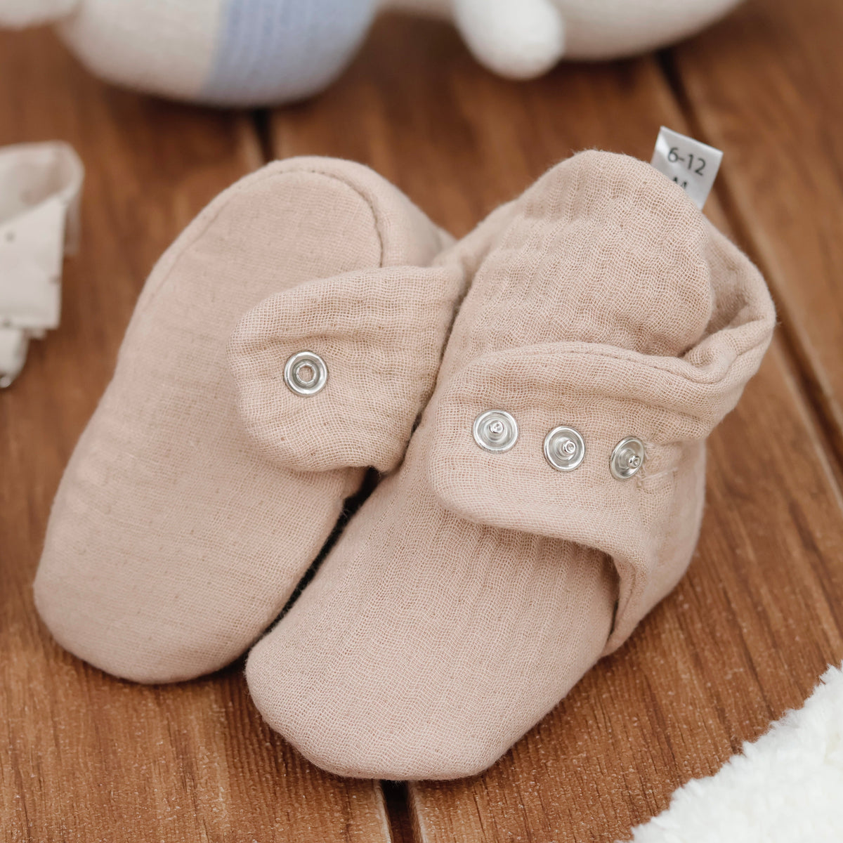 Close-up of beige textured muslin baby booties with snap straps, showing one sole and an open snap strap.