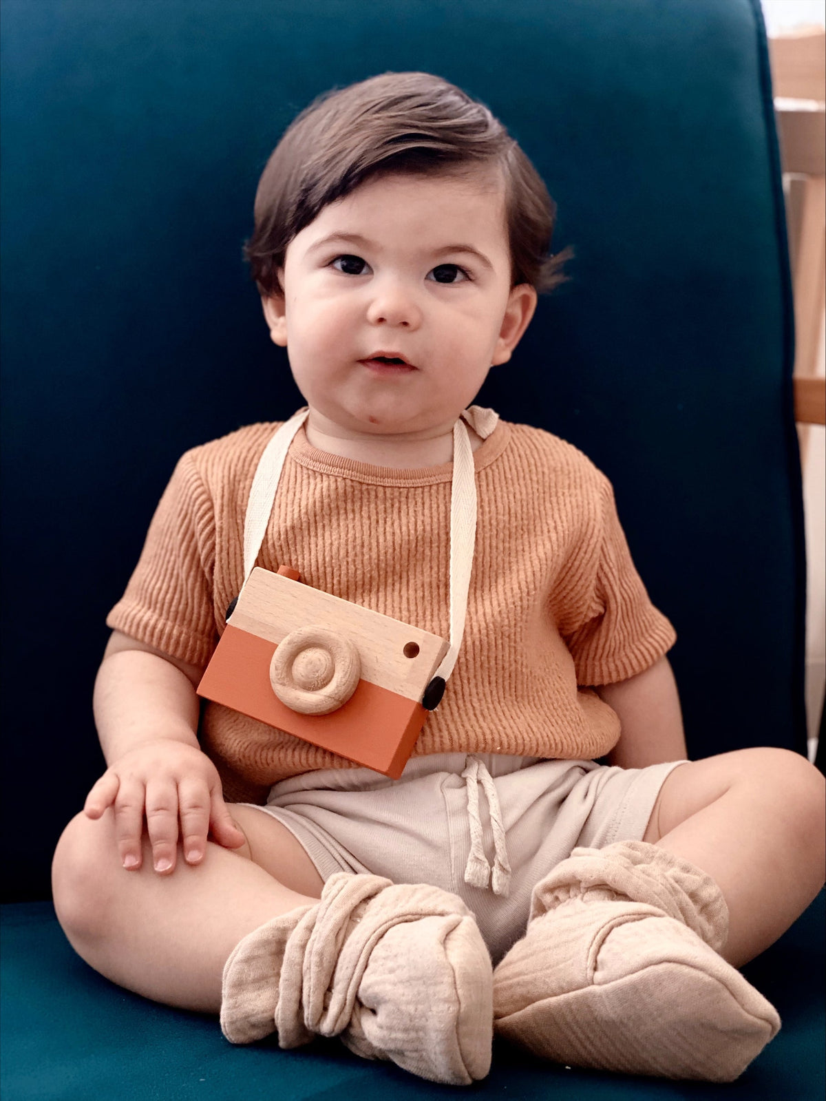 Baby seated in a teal chair wearing beige muslin booties.