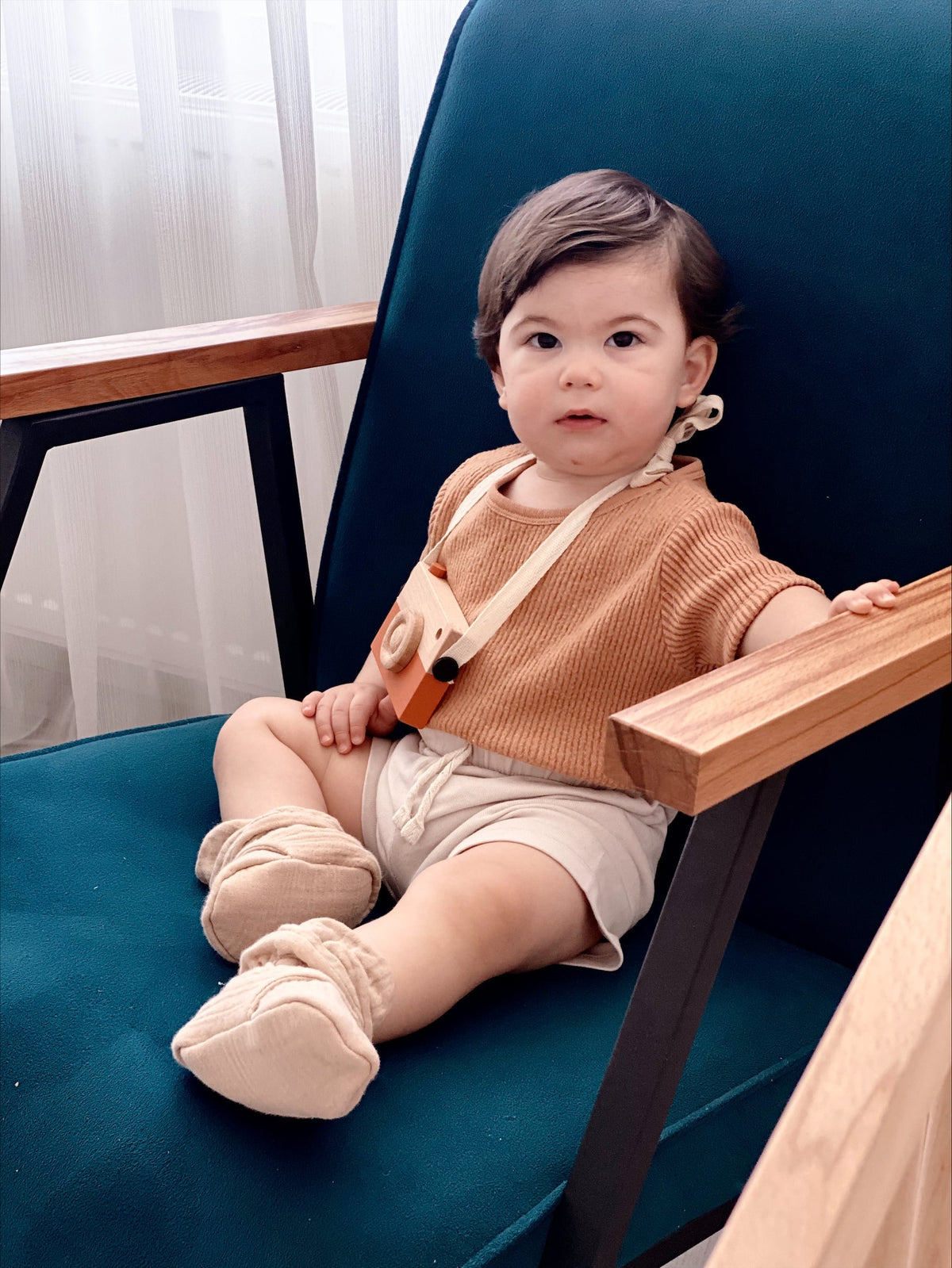 Baby reclining in a teal chair wearing beige muslin booties.
