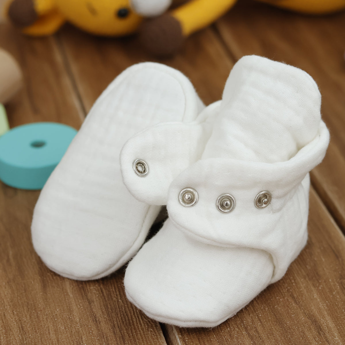 Close-up of cream textured muslin baby booties with snap straps, showing one sole and an open snap strap.