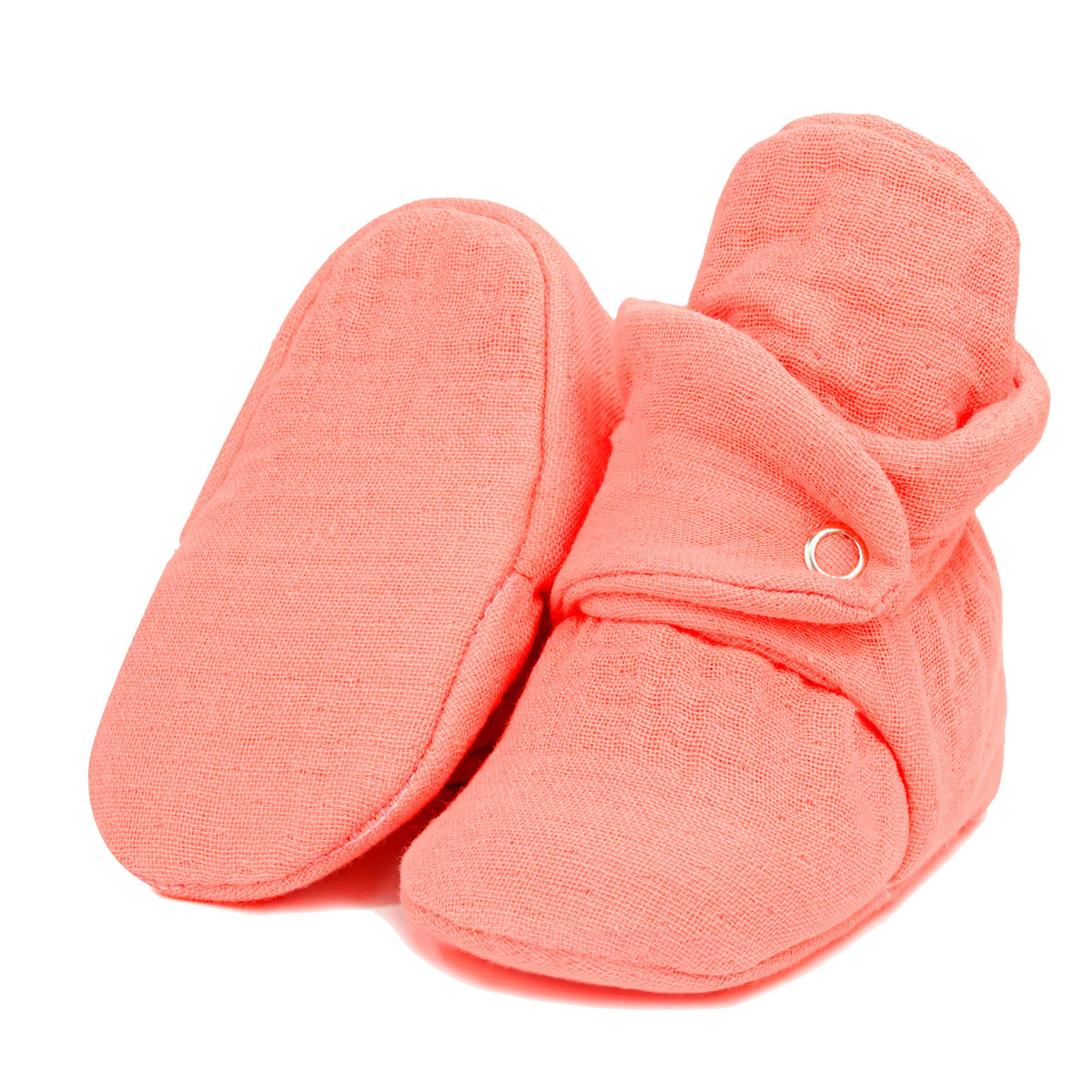 Dusty coral pink textured muslin baby booties with snap straps, with one sole facing the camera on a white background.
