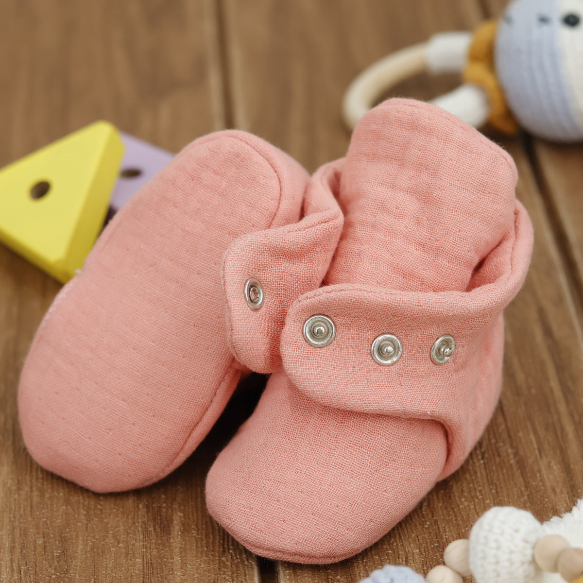 Close-up of dusty coral pink textured muslin baby booties with snap straps, showing one sole and an open snap strap.