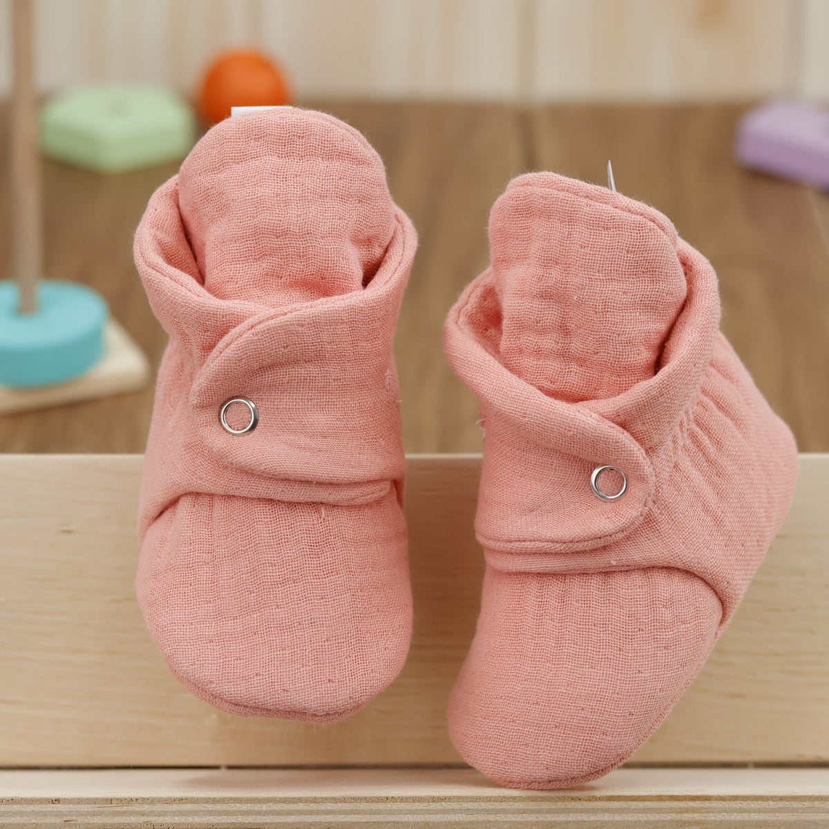Front view of a pair of dusty coral pink textured muslin baby booties with snap straps.