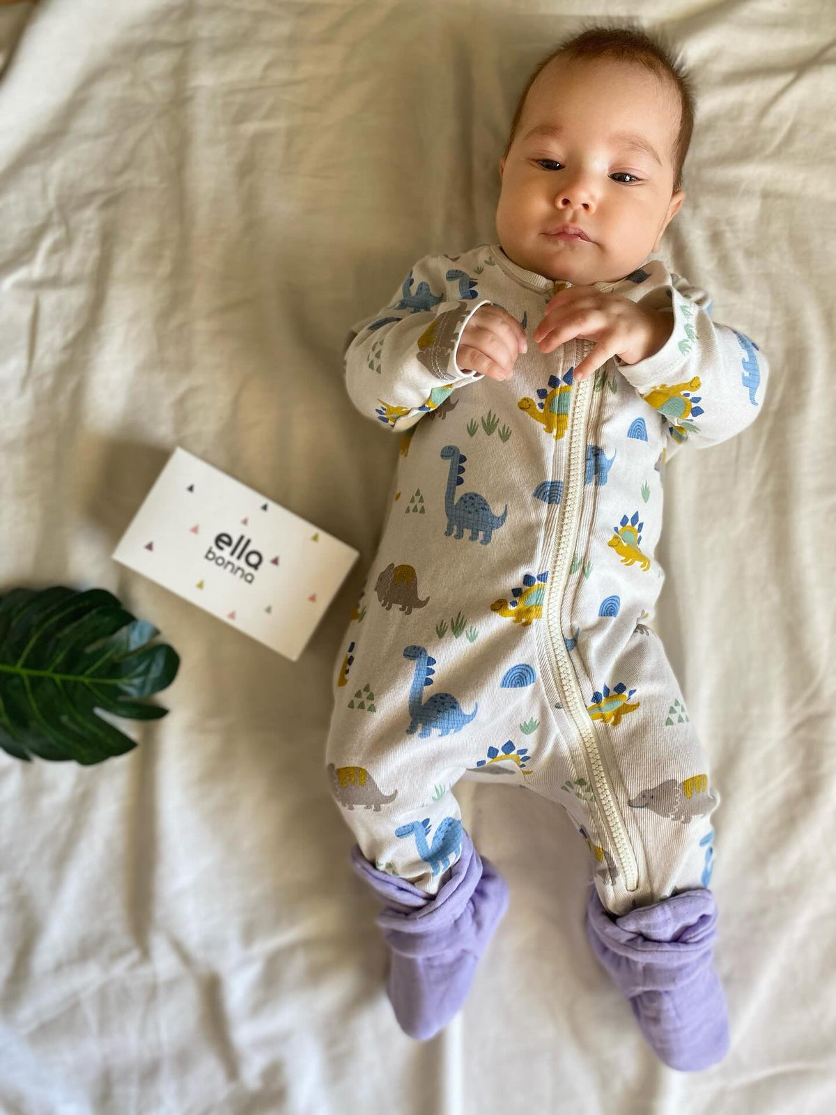 Baby lying on a blanket wearing lilac booties beside an Ella Bonna card.