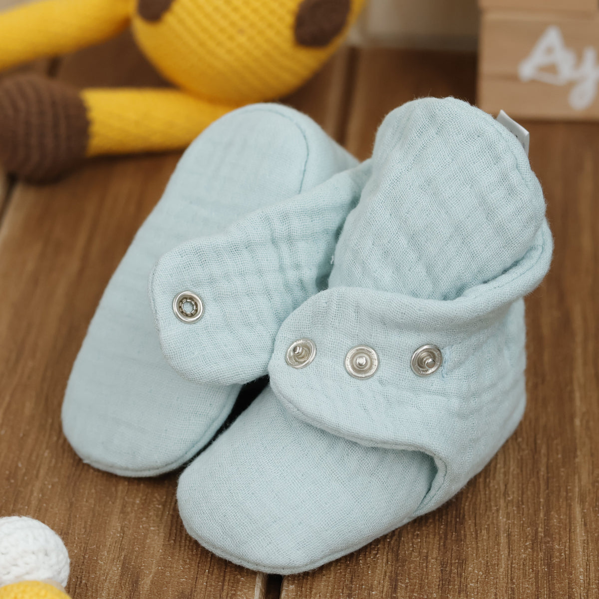 Close-up of mint textured muslin baby booties with snap straps, showing one sole and an open snap strap.