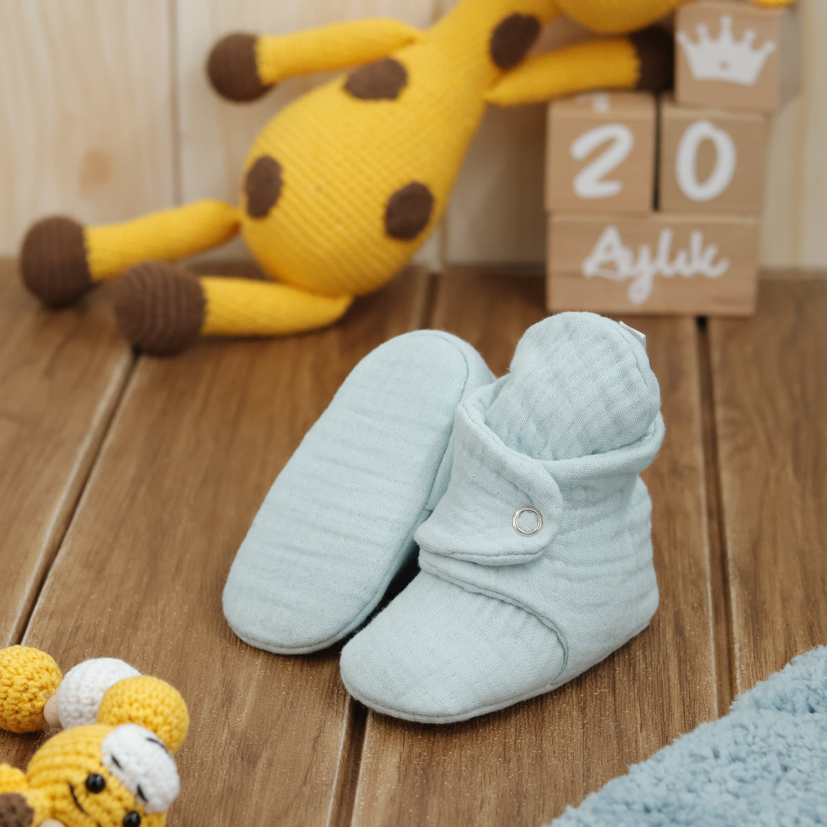 Mint textured muslin baby booties with snap straps arranged on a surface with one sole facing the camera.