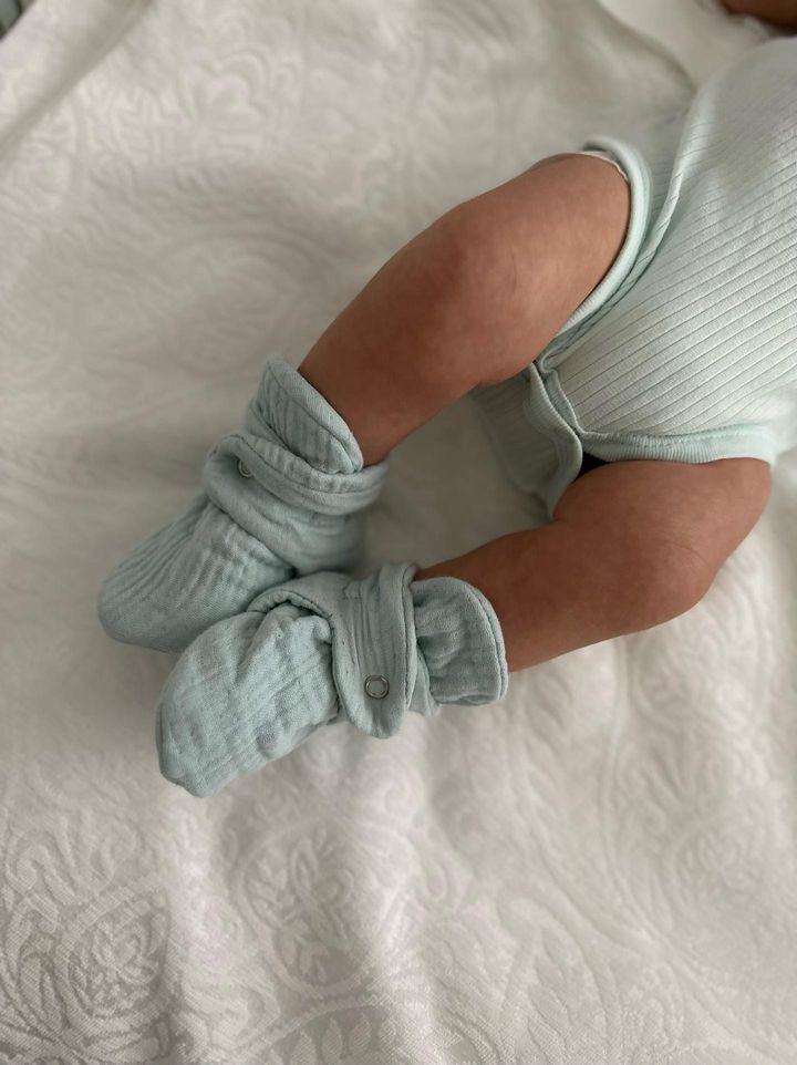 Side close-up of mint booties worn by a baby lying on a blanket.