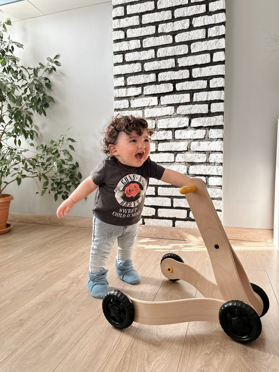 Child standing with a wooden walker wearing blue booties.