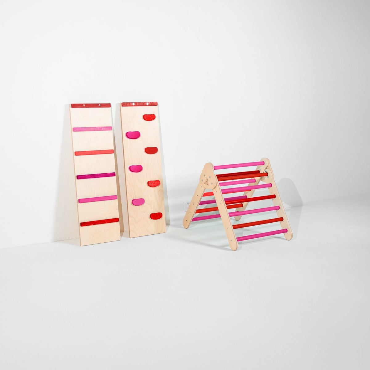 Small red and pink climbing triangle beside upright ladder and climbing-hold ramps.