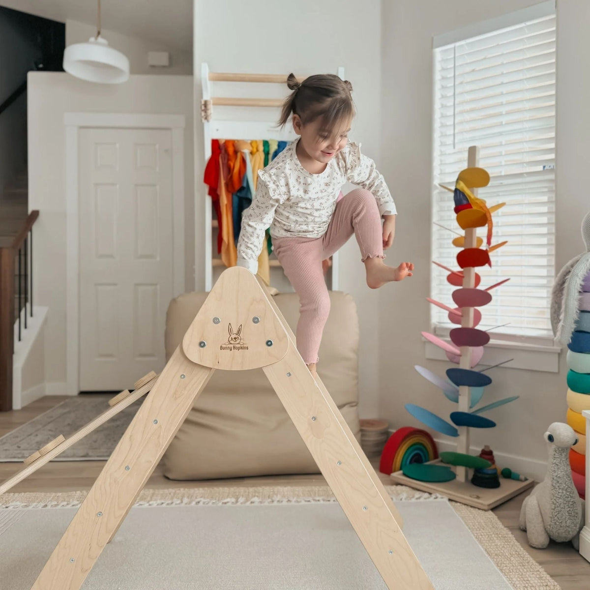 Child lifting one leg over the top of a pale natural-tone climbing triangle.