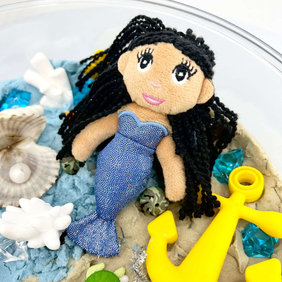 Tan-skinned fabric mermaid doll with black hair and blue tail; the yellow anchor shown is not included