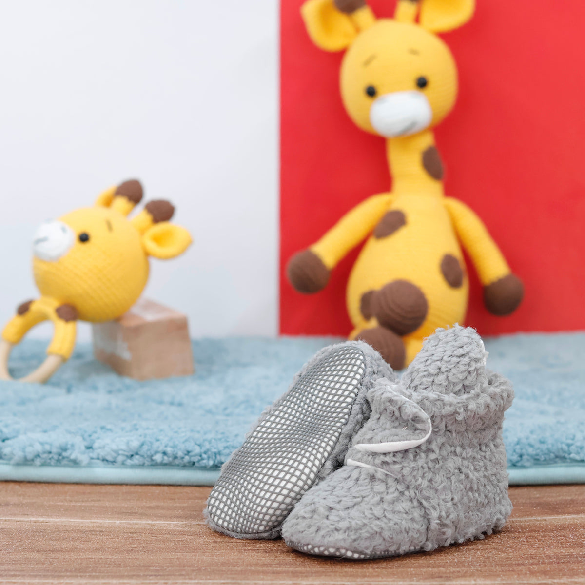 Gray teddy-texture baby booties with snap straps and gray grip soles arranged on a surface with one sole facing the camera.