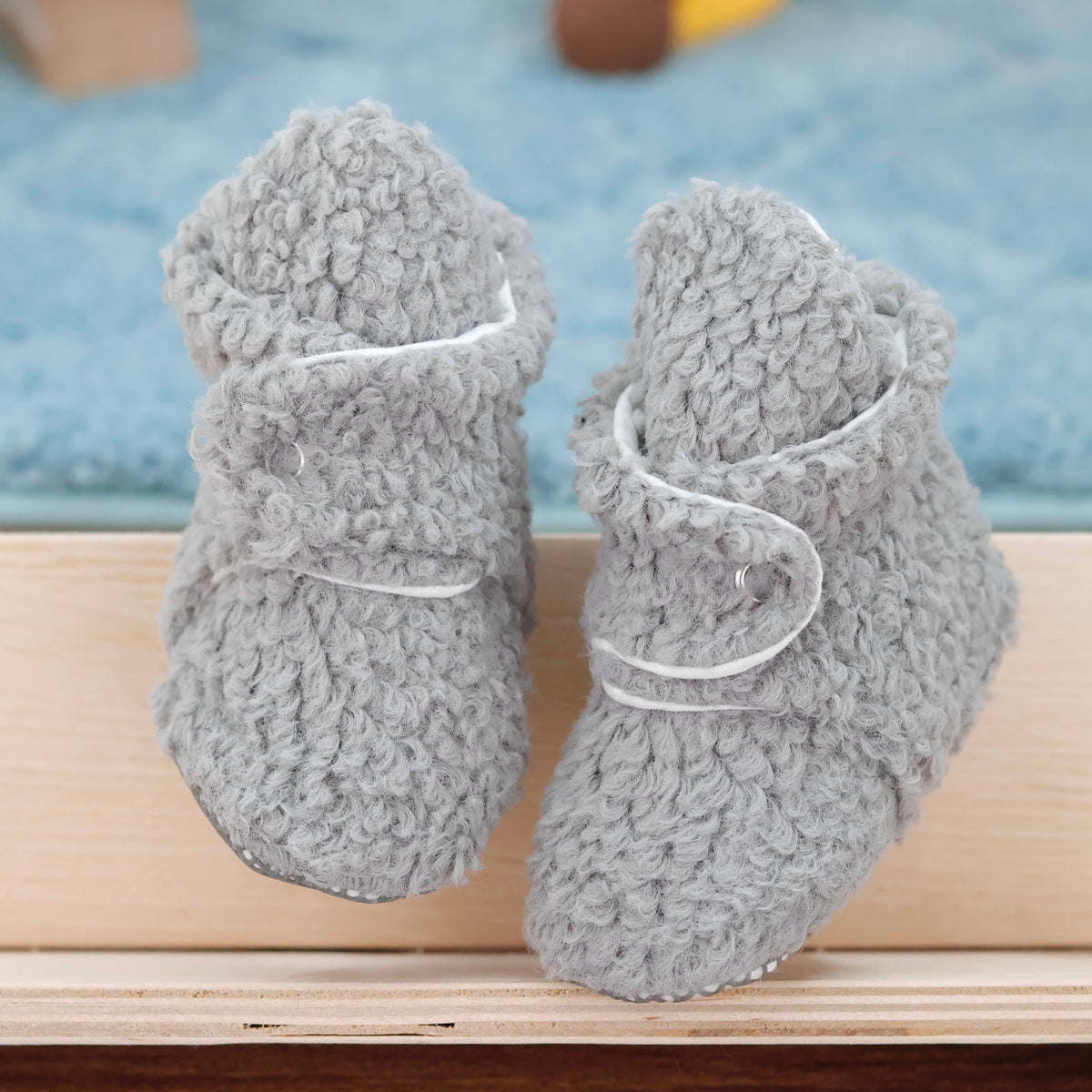 Front view of a pair of gray teddy-texture baby booties with snap straps and gray grip soles.