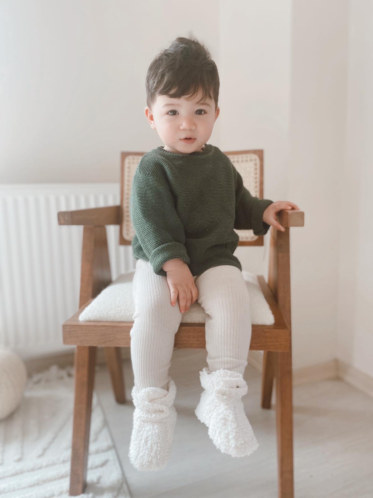 Front view of a child seated on a chair wearing white teddy booties.