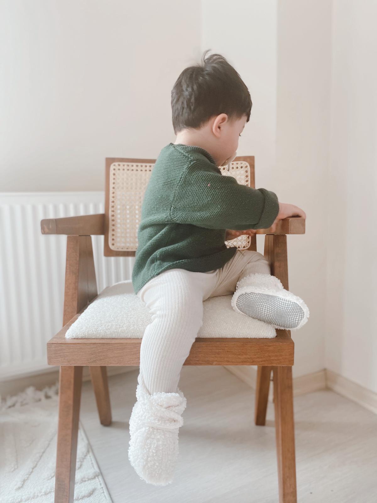 Child seated sideways on a chair wearing white teddy booties.