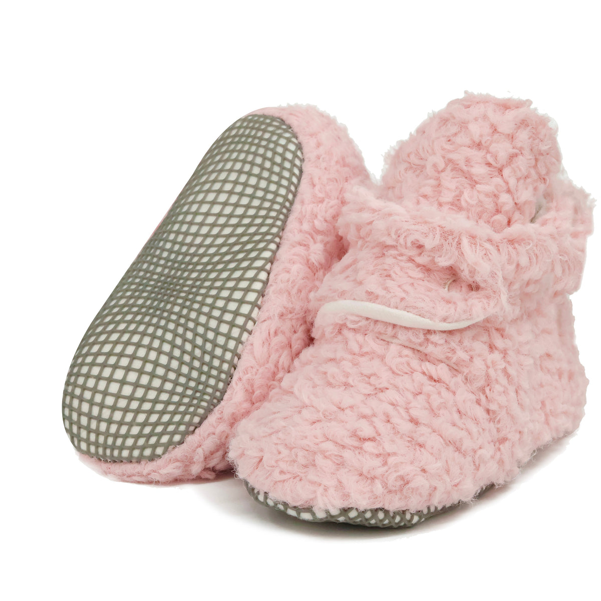 Pink teddy-texture baby booties with snap straps and gray grip soles, with one sole facing the camera on a white background.