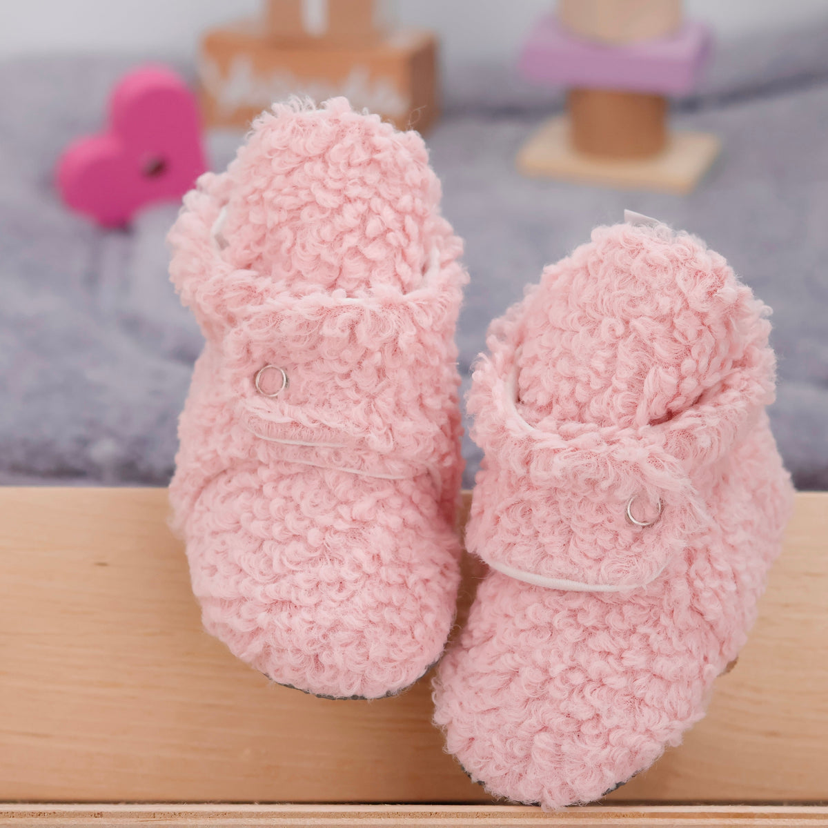 Front view of a pair of pink teddy-texture baby booties with snap straps and gray grip soles.