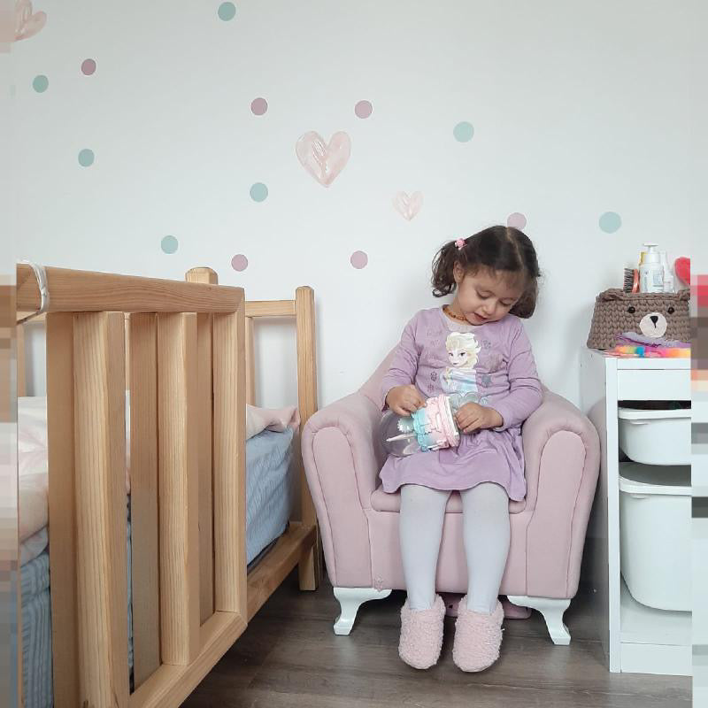 Child seated in a pink chair wearing pink teddy booties.