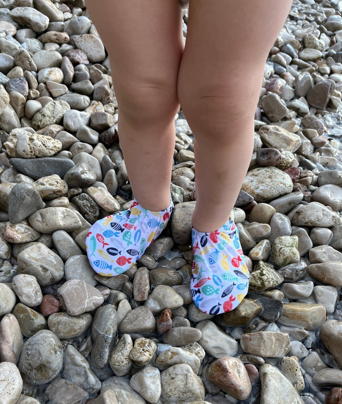 Close-up of colorful fish-print water shoes worn on a pebble beach.